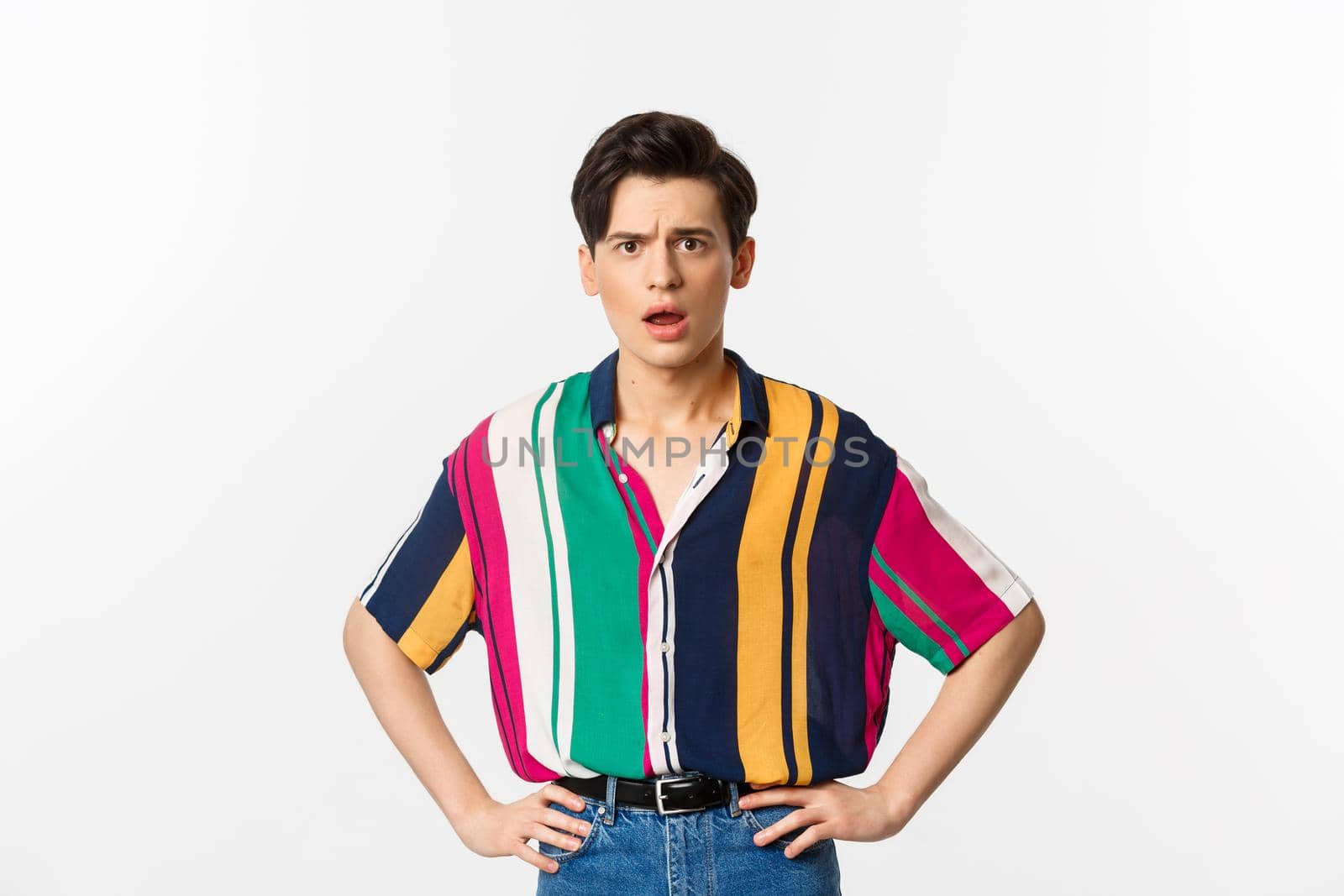 Image of confused and upset young man staring at camera, standing disappointed over white background.