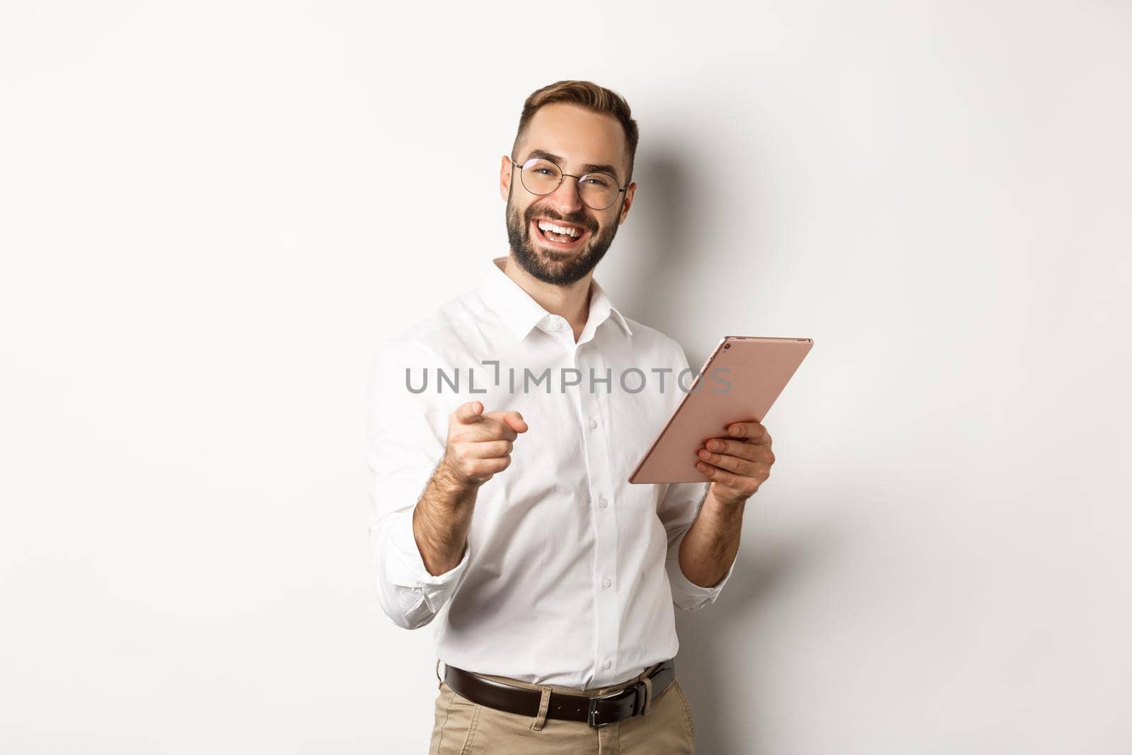 Happy and satisfied boss praising good job, reading on digital tablet and pointing at you camera, standing over white background.