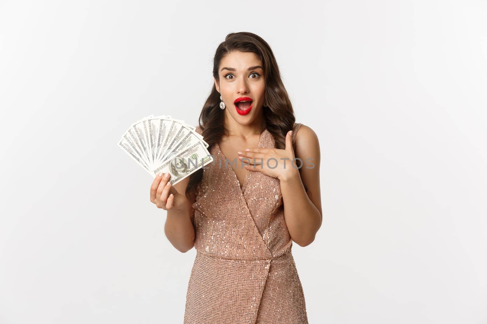 Shopping concept. Elegant woman in glamour dress holding money and looking surprised. winning prize, standing over white background.
