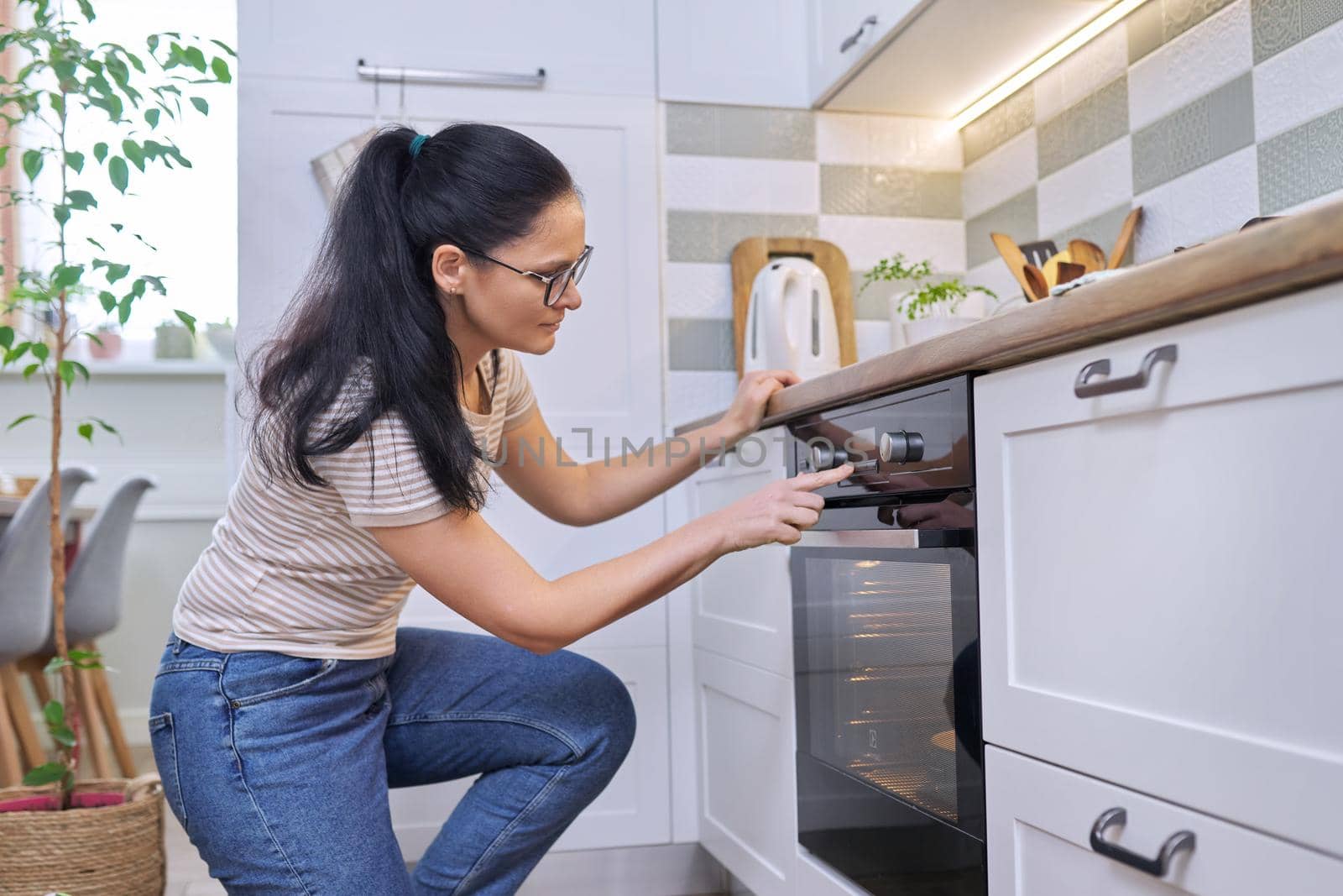 Middle aged woman cooking pie in the oven at home in the kitchen. Food, eating at home, lifestyle, 40s people concept