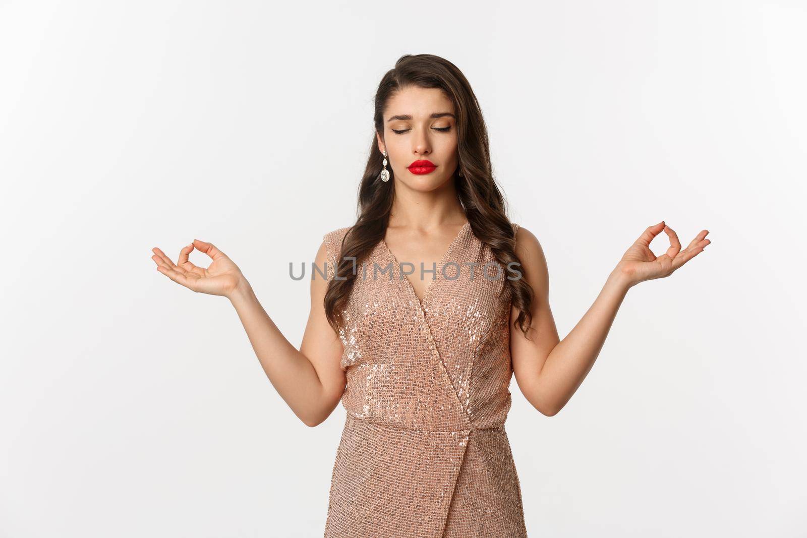 Christmas party and celebration concept. Calm and patient young woman in stylish dress meditating, feeling zen, standing over white background.