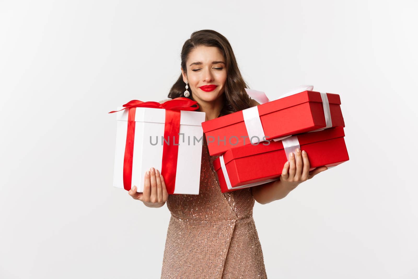 Holidays, celebration concept. Beautiful caucasian woman in elegant dress holding Christmas presents and smiling happy, standing over white background.