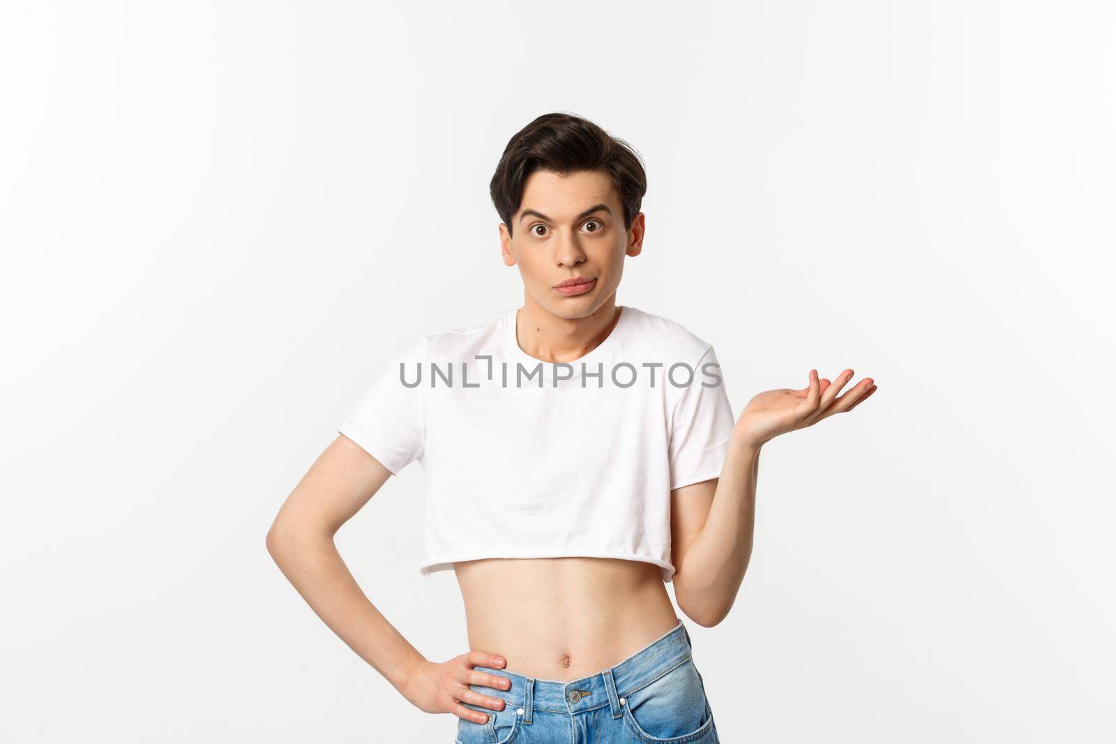 Handsome androgynous man in crop top looking confused, shrugging clueless, standing over white background.