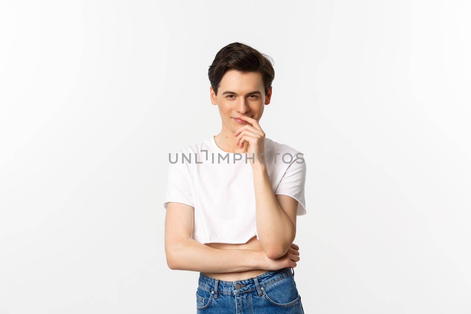 Lgbtq and pride concept. Satisfied young gay man thinking, having an idea and smiling while staring at camera, wearing crop top, white background.