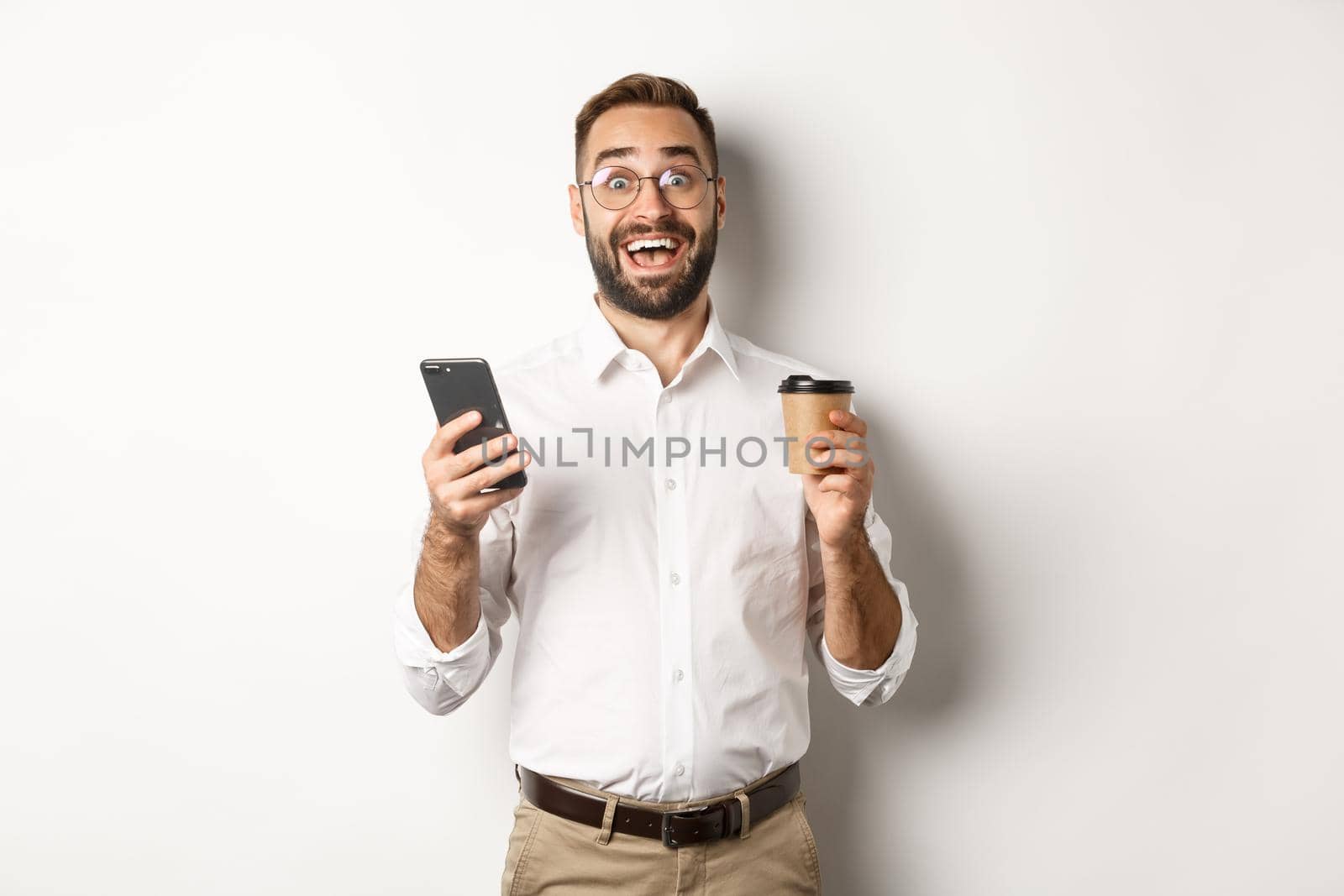 Amazed businessman drinking coffee, reacting at awesome online offer on mobile phone, standing over white background.
