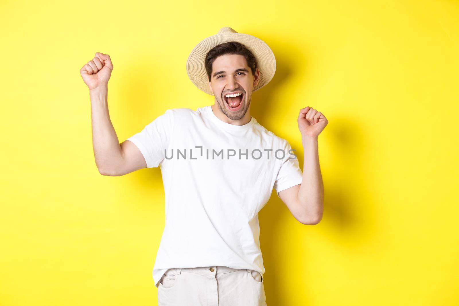 Concept of tourism and lifestyle. Happy man tourist celebrating, rejoicing over vacation, standing over yellow background.