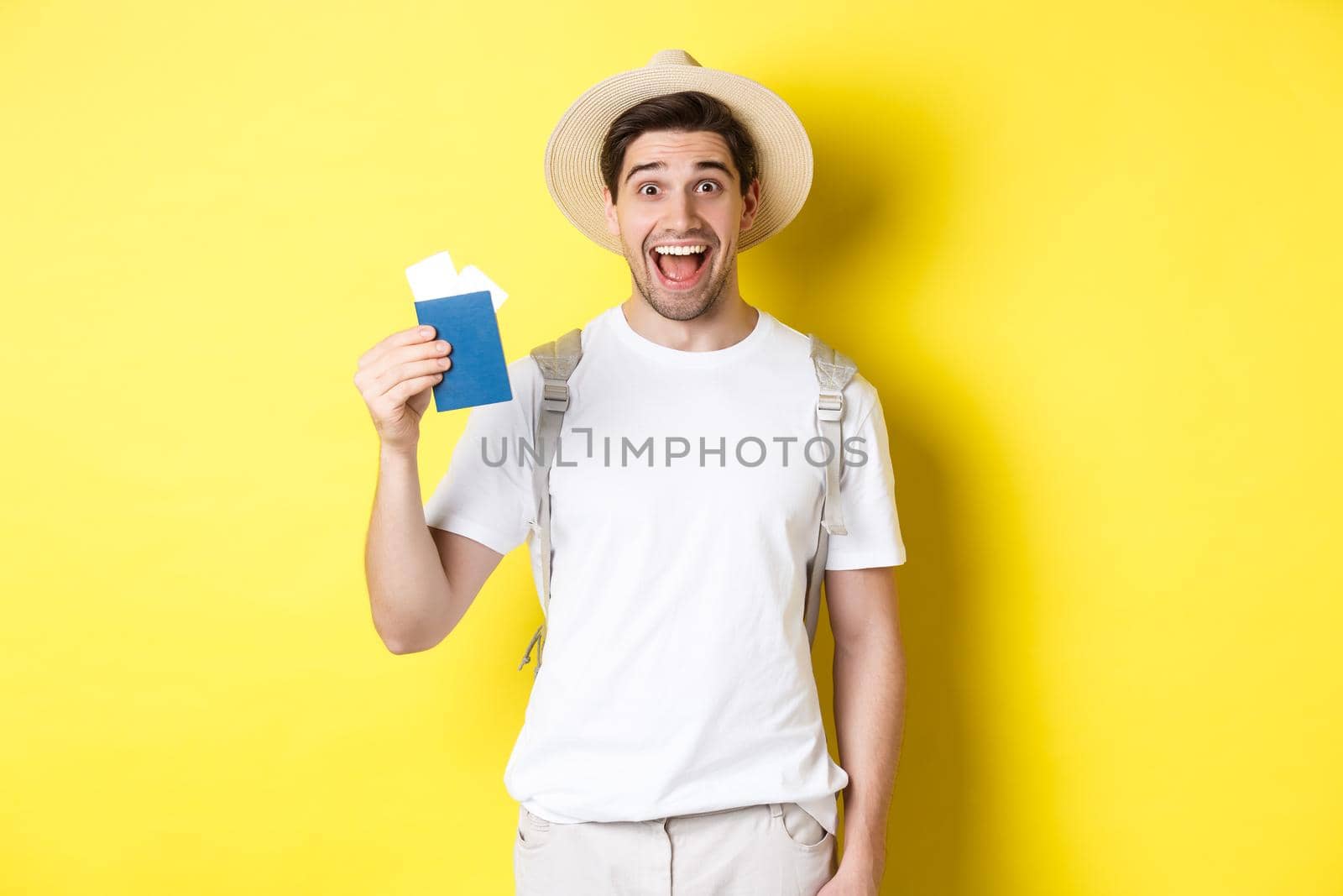 Tourism and vacation. Happy man tourist showing his passport with tickets, going on journey, standing over yellow background with backpack.