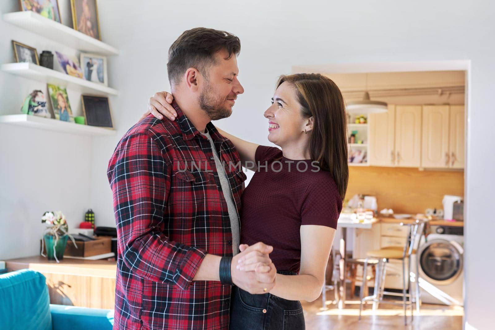 Happy romantic middle aged couple dancing at home. Loving husband and wife 40s of age are embracing and dancing in the living room. Family, relationship, date, mature age concept