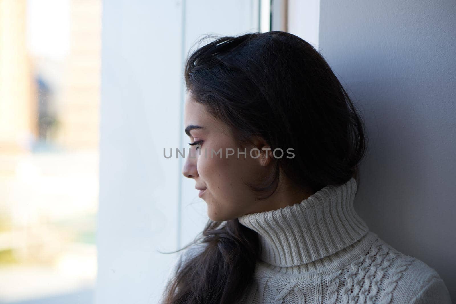 brunette in a white sweater looks out the window pensive view. High quality photo