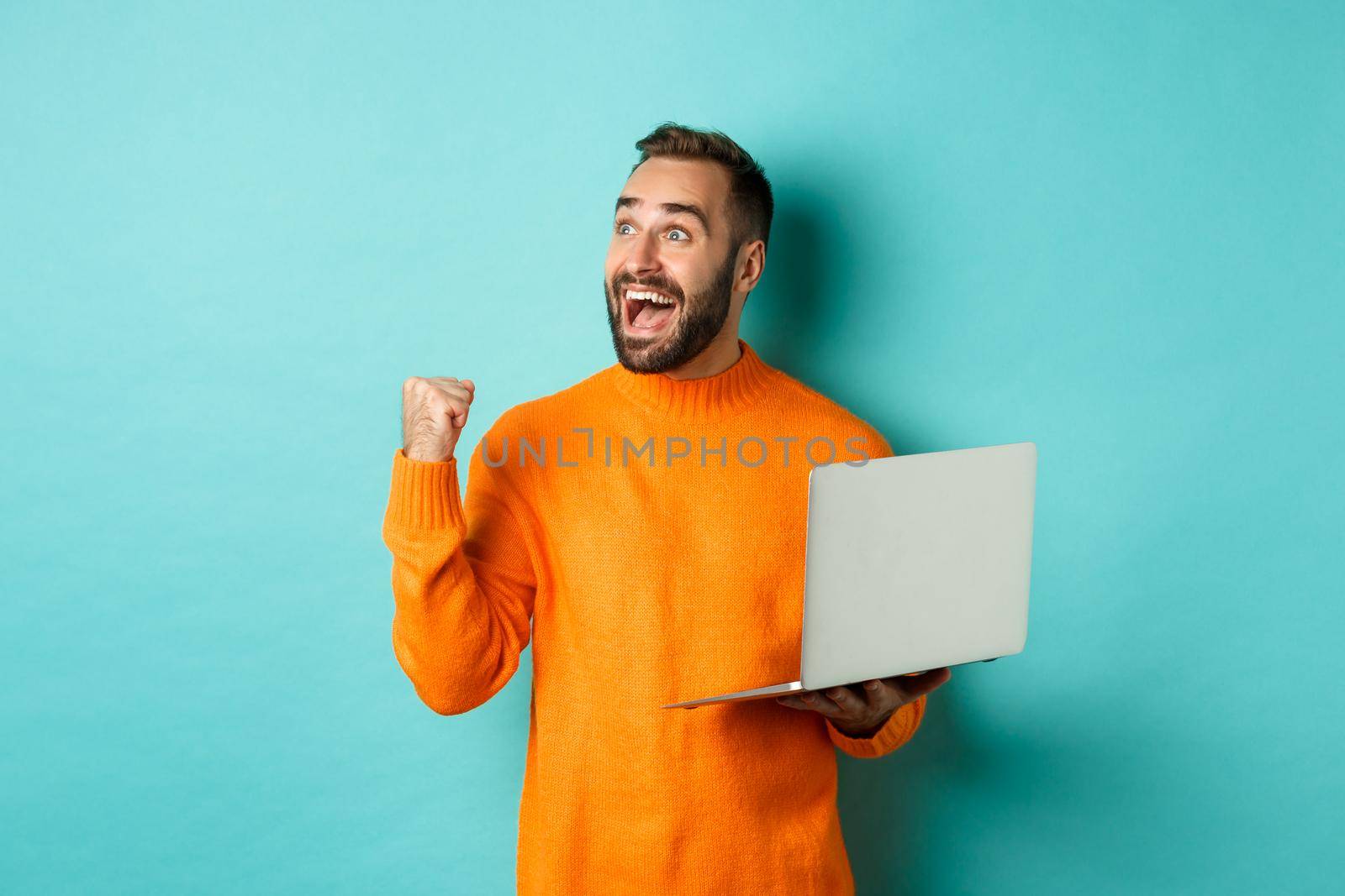 Freelance and technology concept. Lucky man winner celebrating, winning online, showing fist pump and holding laptop, looking at upper left corner.
