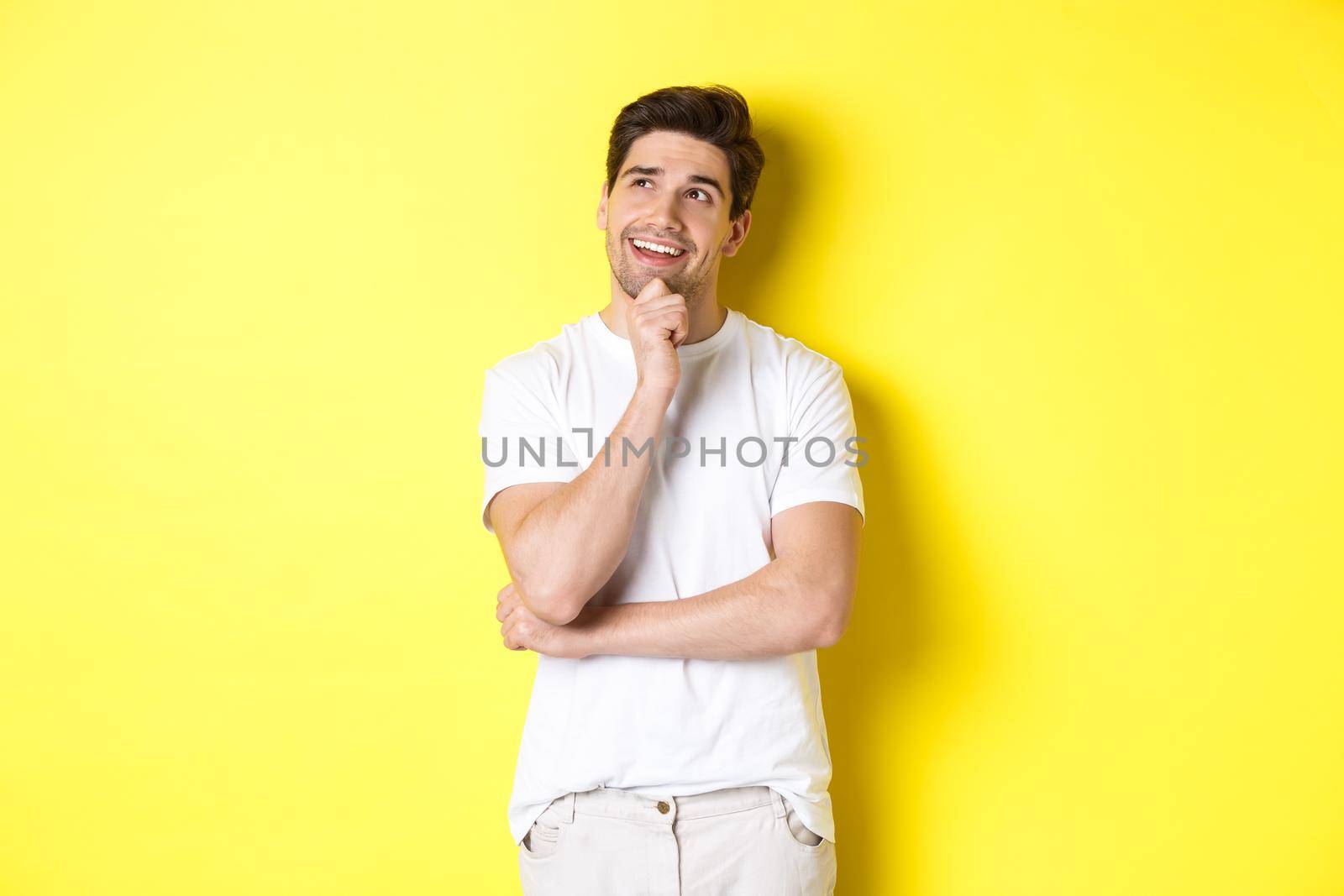 Portrait of smiling man looking thoughtful at upper left corner, choosing something, have an idea, standing against yellow background by Benzoix