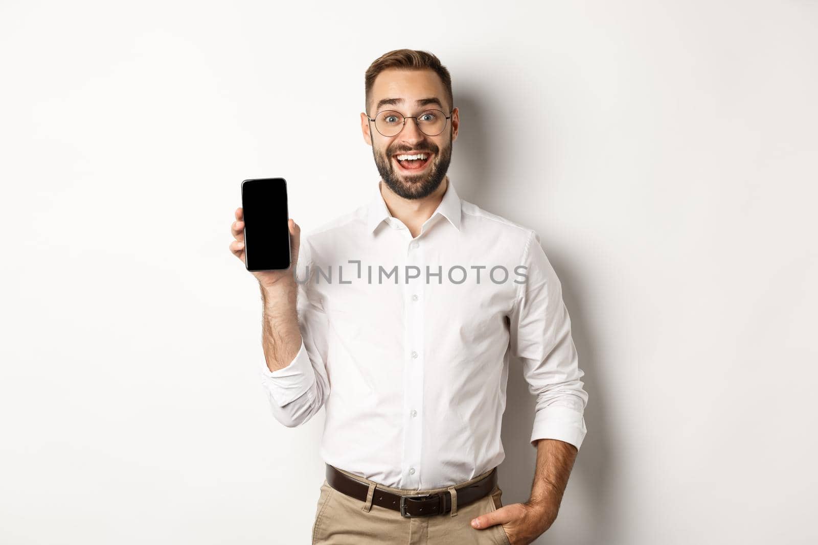 Amazed handsome businessman showing smartphone screen app, standing over white background by Benzoix