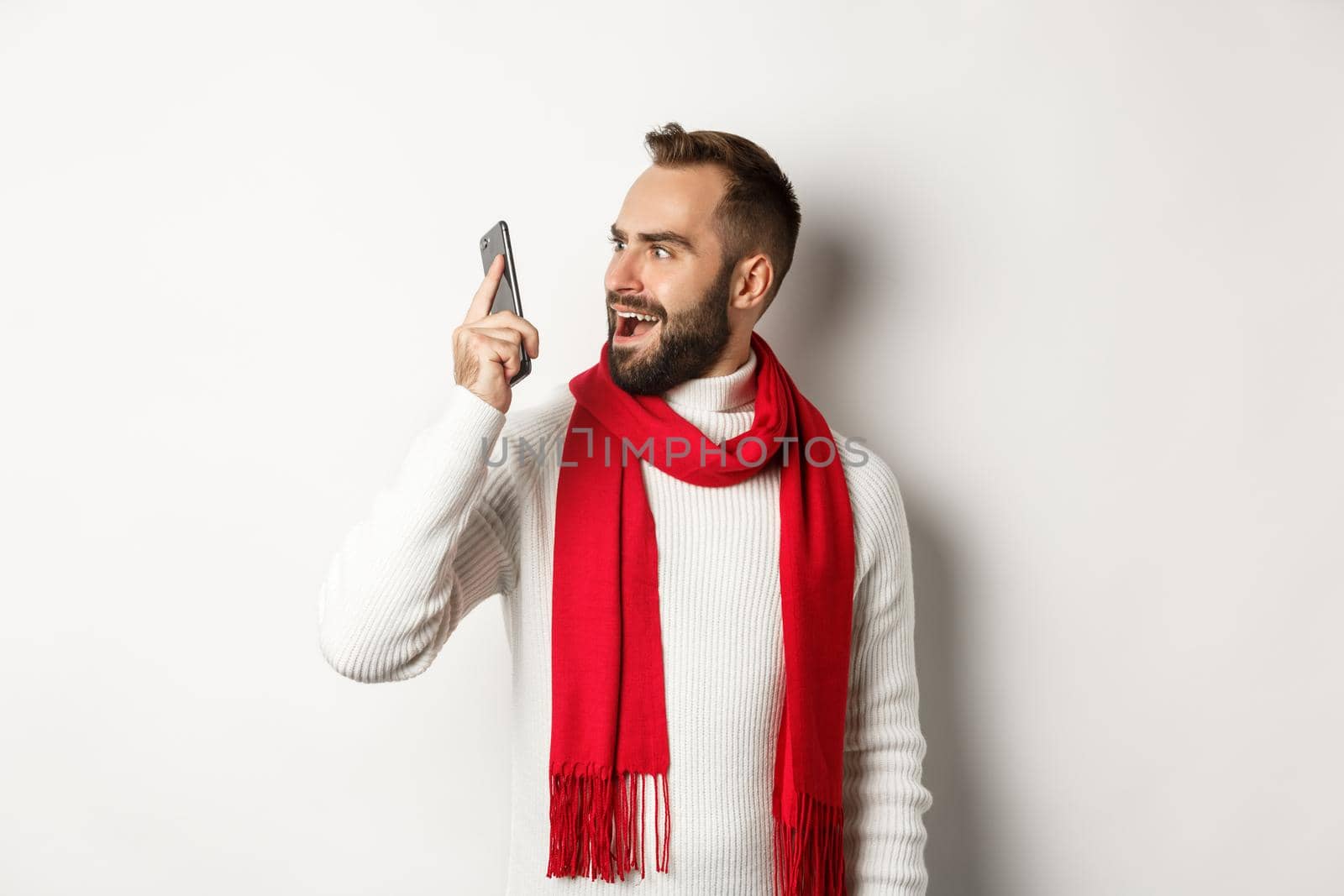 Man looking confused at mobile phone after hearing strange voice, stare at smartphone shocked, standing over white background.