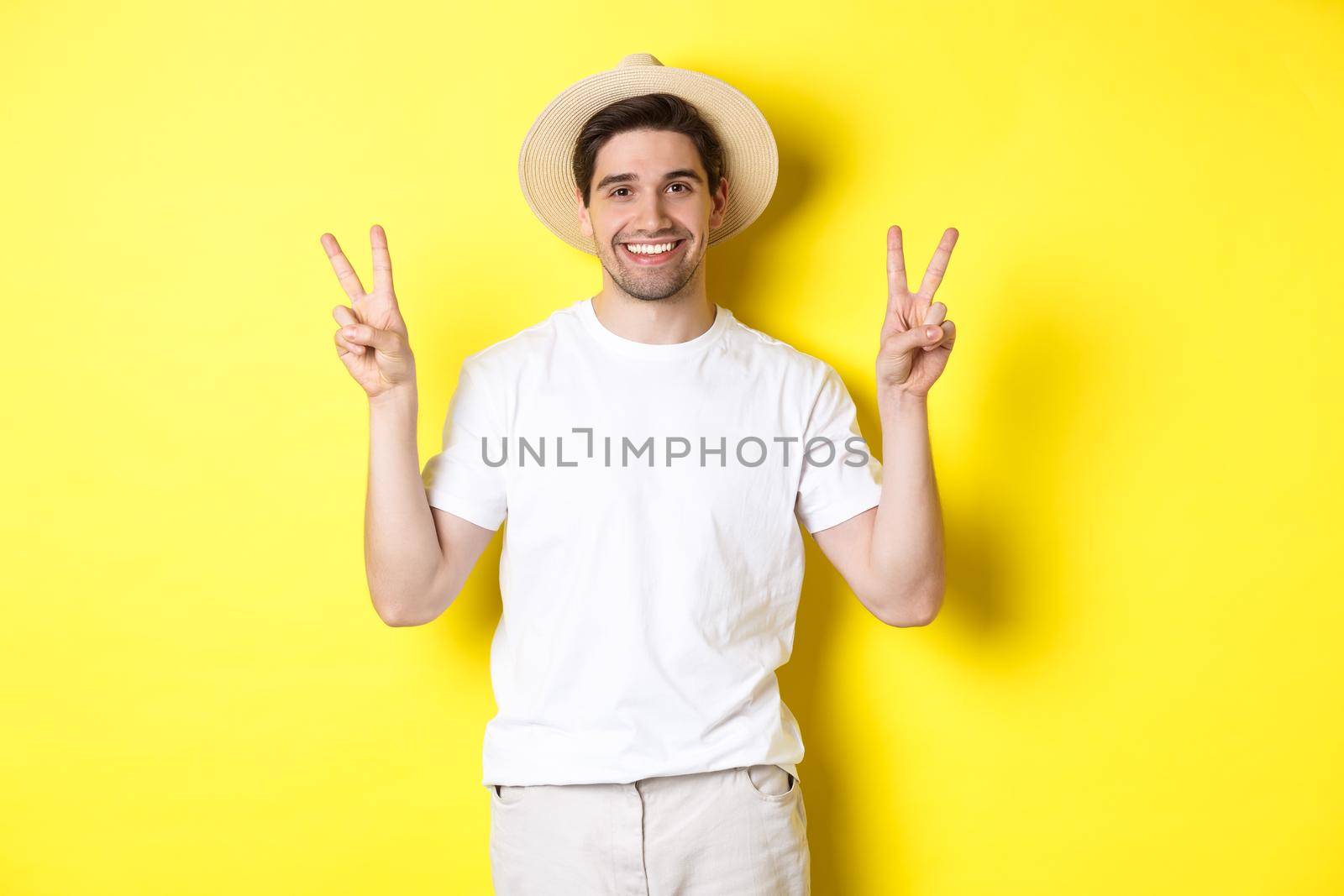 Concept of tourism and vacation. Happy male tourist posing for photo with peace signs, smiling excited, standing against yellow background by Benzoix