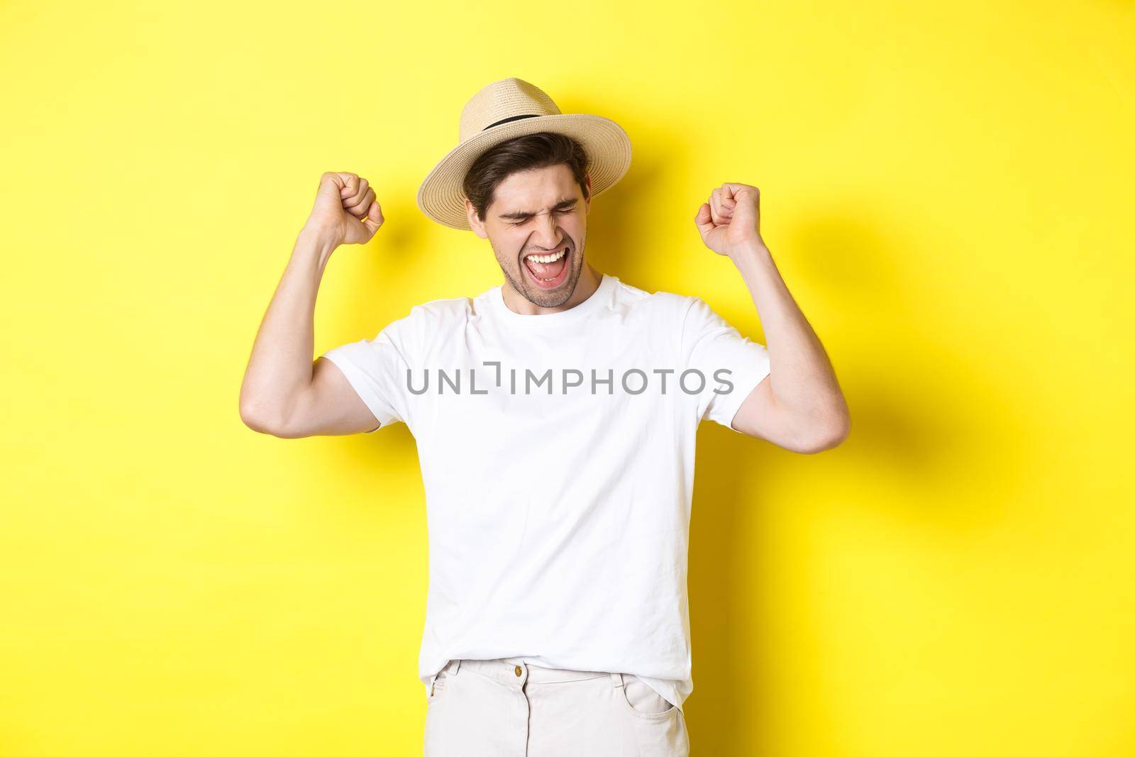 Concept of tourism and vacation. Happy man rejoicing, winning something or achieve goal, triumphing against yellow background by Benzoix