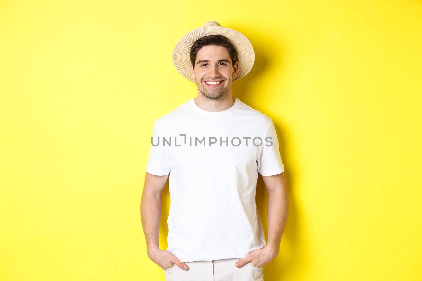 Young handsome guy tourist looking happy, wearing straw hat for travelling, standing against yellow background by Benzoix