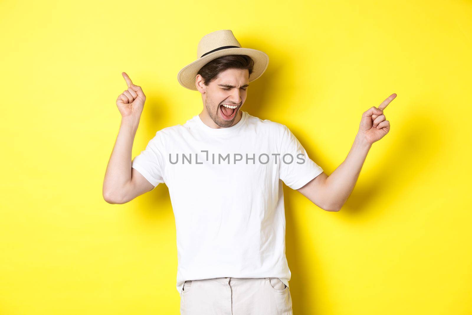 Concept of tourism and lifestyle. Happy man enjoying vacation, tourist dancing over yellow background by Benzoix