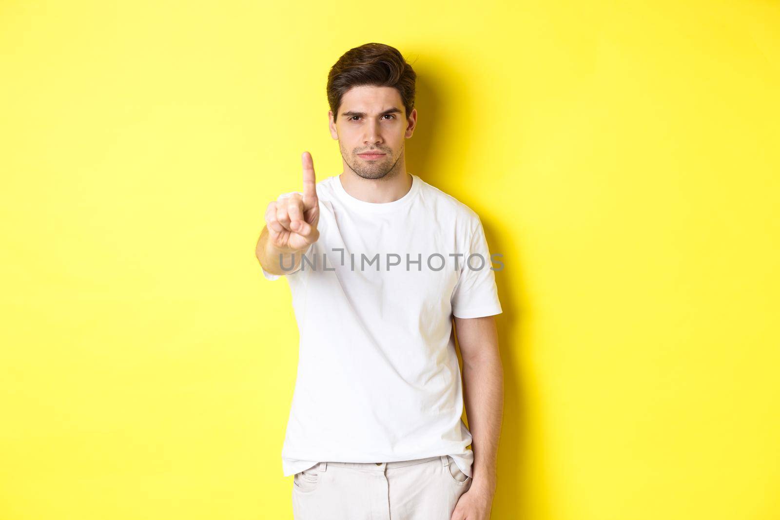 Confident man saying no, decline and prohibit something, showing one finger and frowning, standing over yellow background by Benzoix
