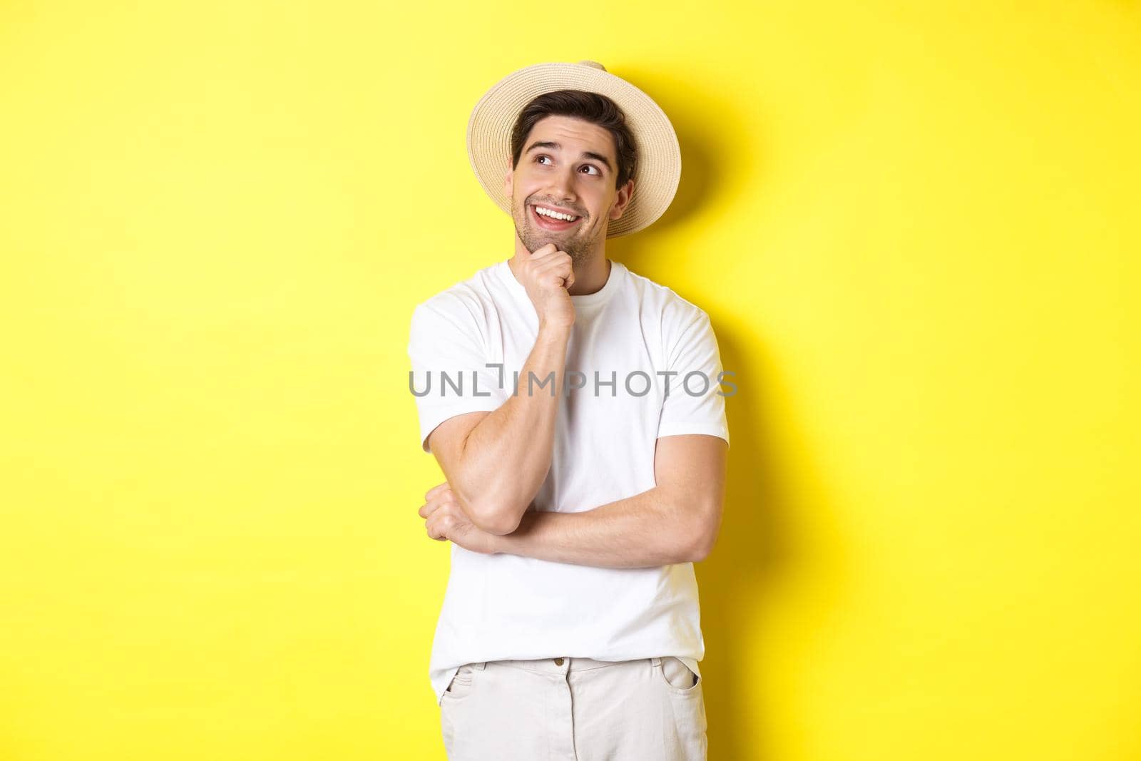 Young thoughtful man tourist imaging something, looking at upper left corner and smiling, thinking and standing over yellow background.