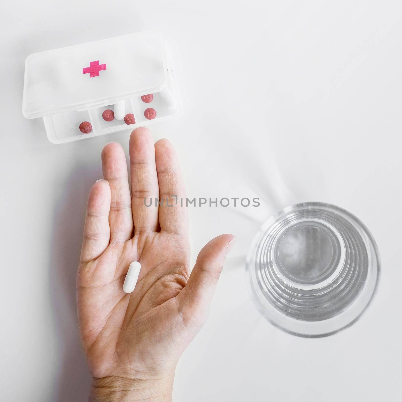person s hand taking tablet from pill organizer box white background. High resolution photo