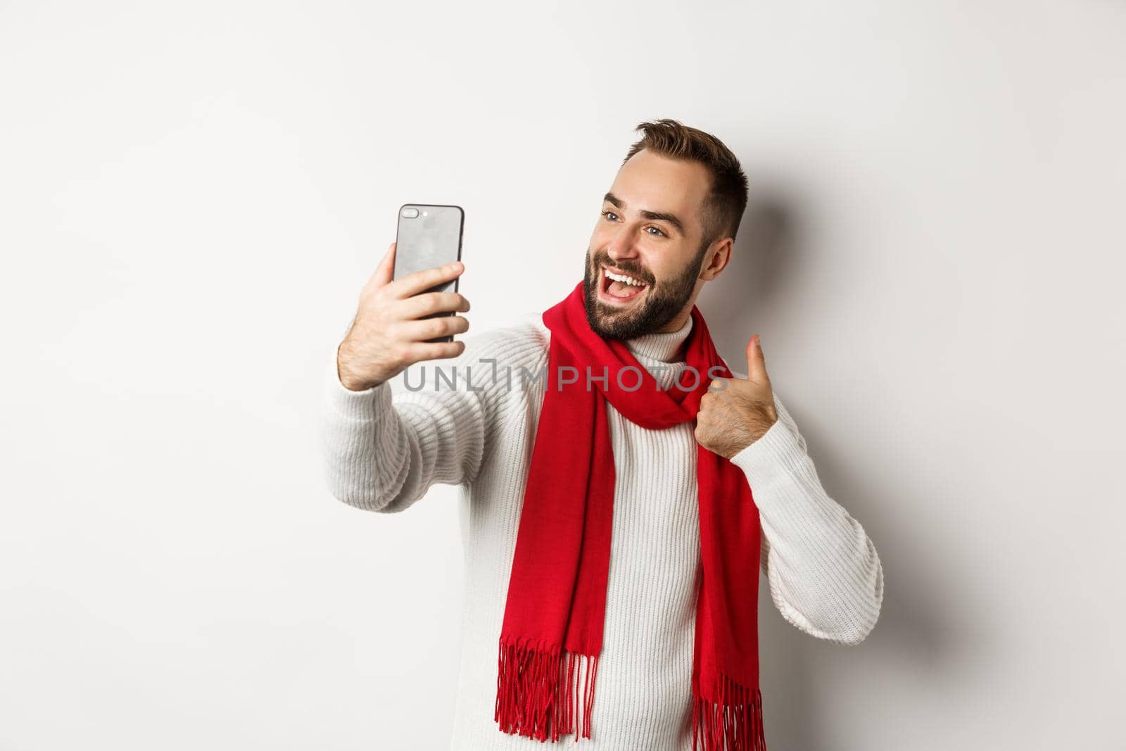 Happy bearded man video call and showing thumbs up at mobile phone, like christmas gift, talking online, standing over white background.