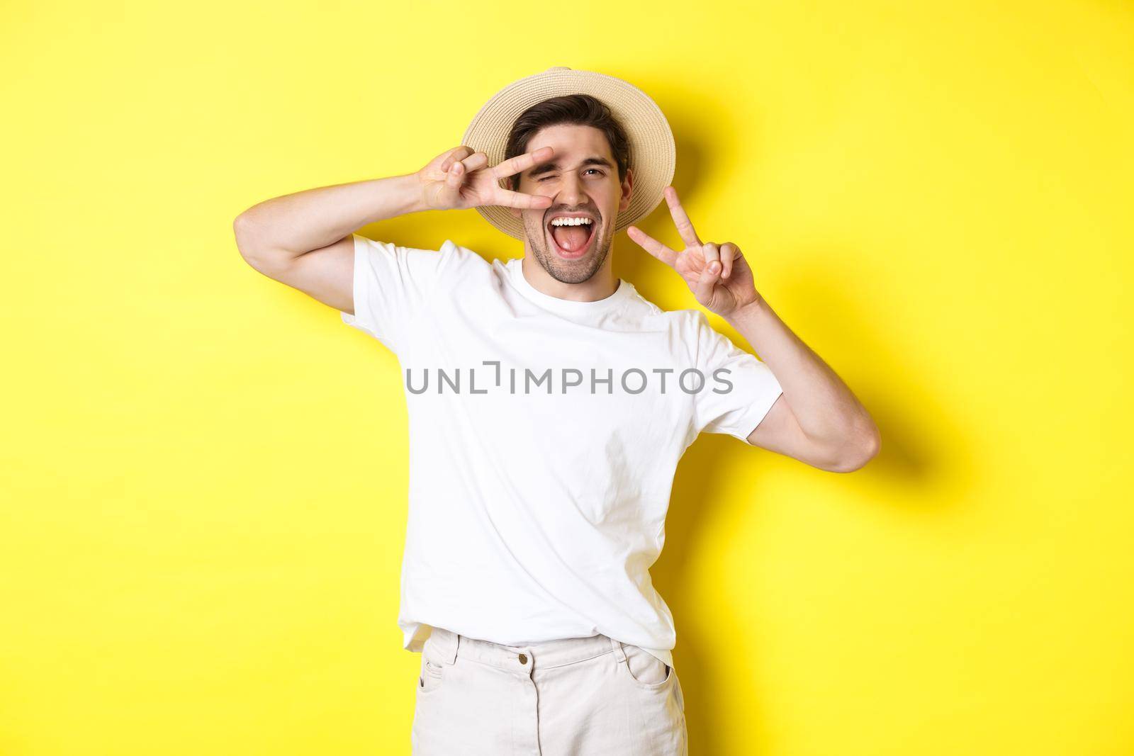 Concept of tourism and vacation. Happy man tourist posing for photo with peace signs, smiling excited, standing against yellow background.