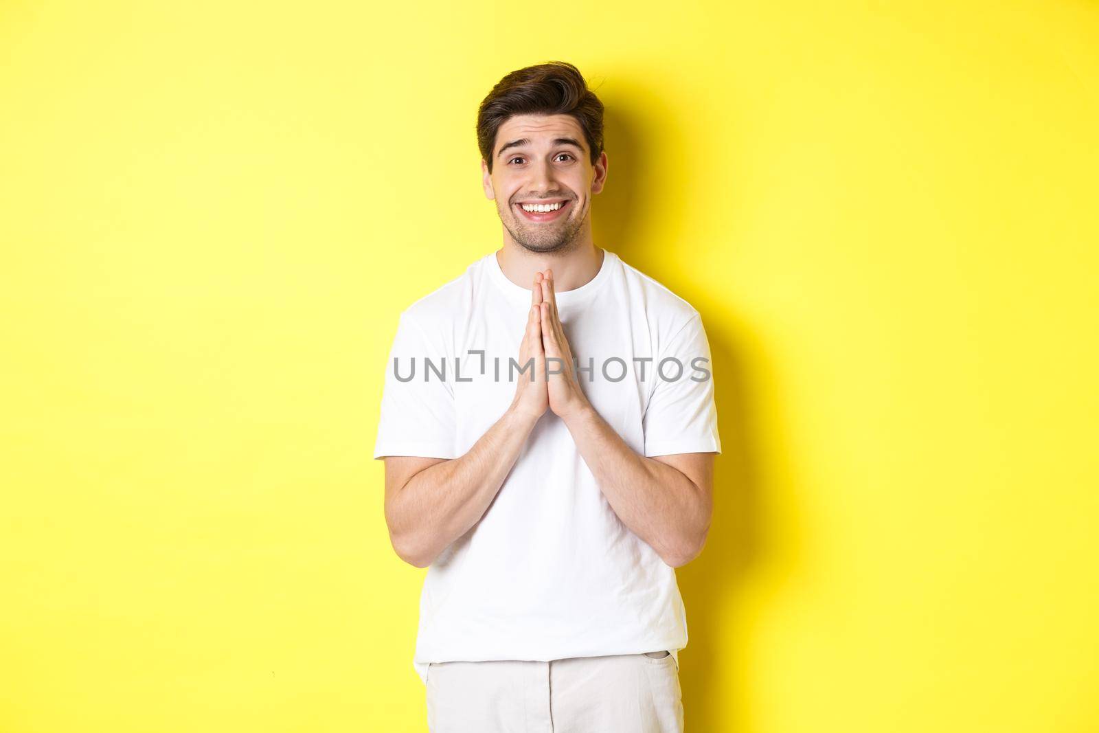 Hopeful man asking for help, begging favour, need something and smiling, standing over yellow background.
