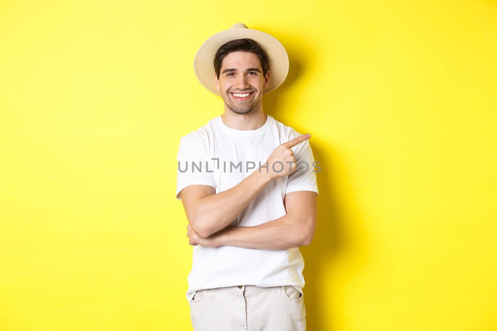 Young male tourist pointing finger right, smiling and showing advertisement, concept of tourism and lifestyle, yellow background.