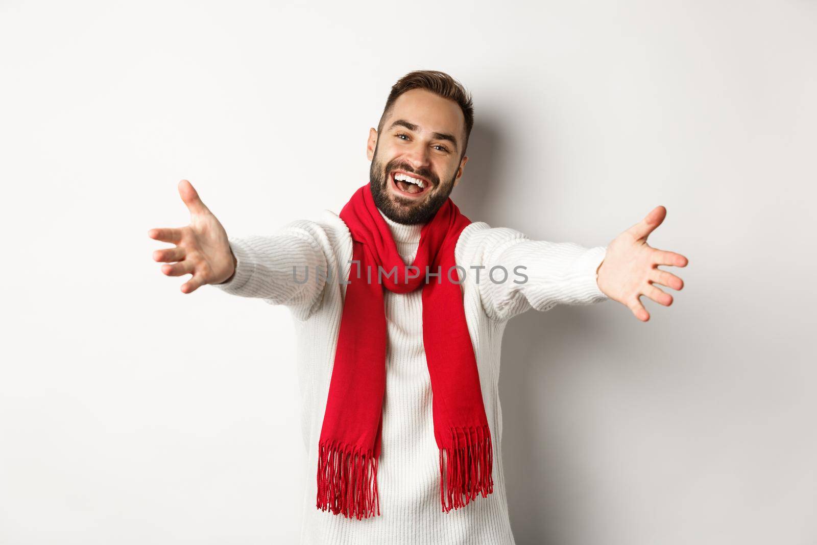Christmas holidays and celebration concept. Friendly man inviting to come in, reaching hands forward in greeting or hug gesture, wishing happy new year, standing over white background.