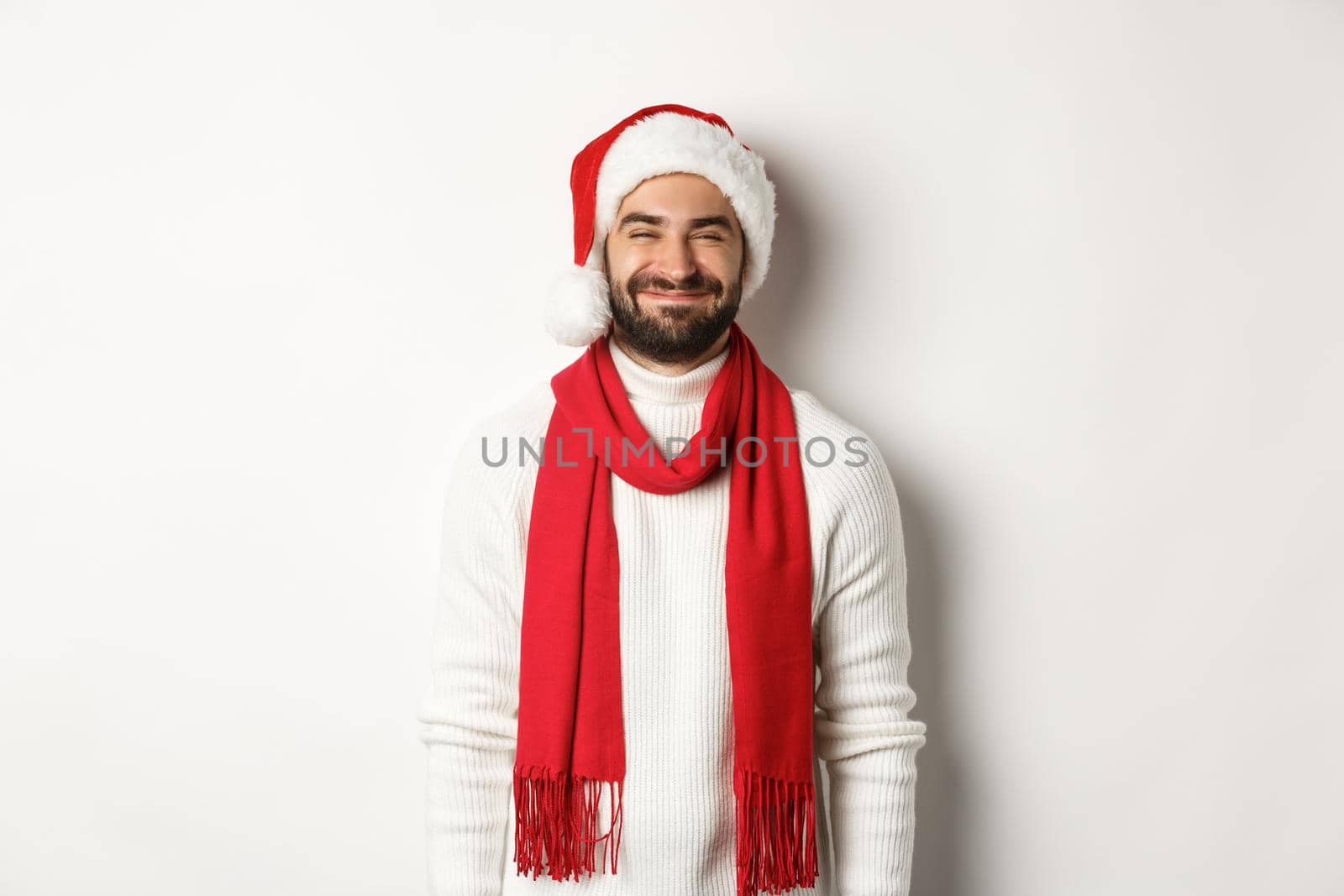 Christmas holidays. Bearded man in santa hat and red scarf looking happy, enjoying New Year party celebration, standing over white background.