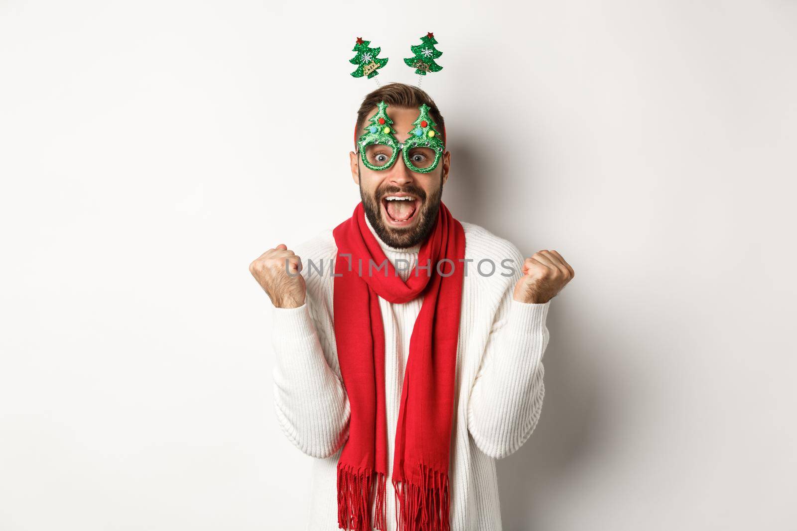 Christmas, New Year and celebration concept. Excited man winning prize, winter promotion, making fist pump and celebrating, wearing party glasses, white background.