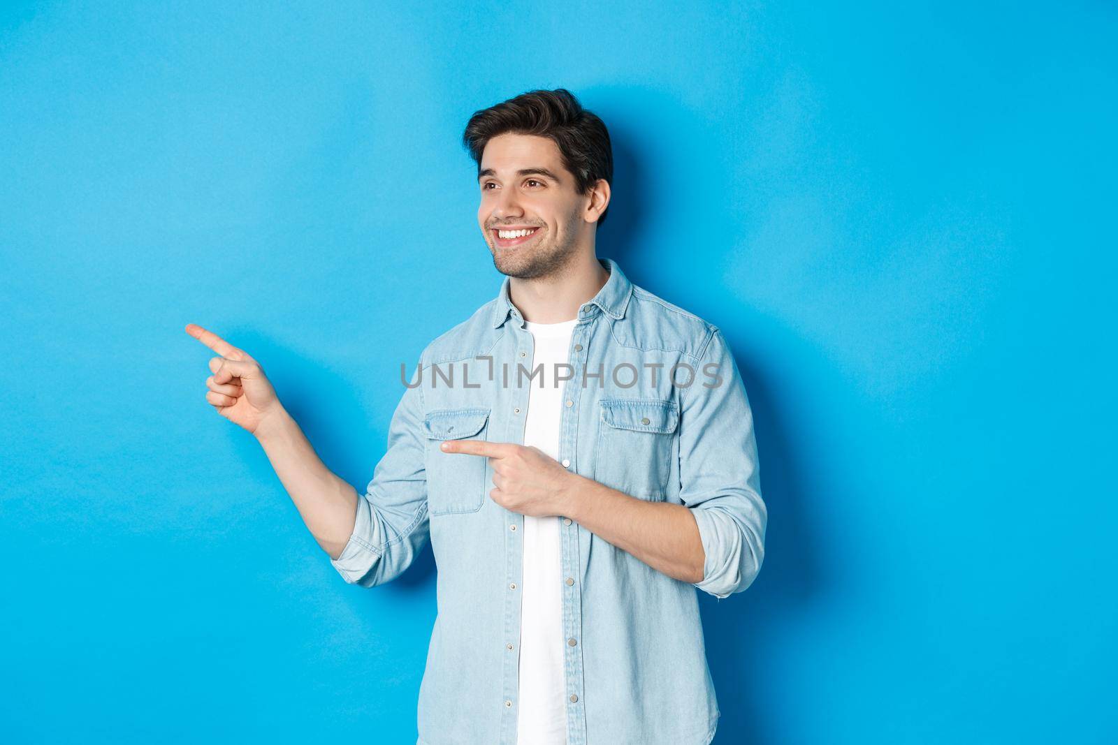 Handsome adult man introduce product, looking and pointing fingers left, promoting something against blue background by Benzoix