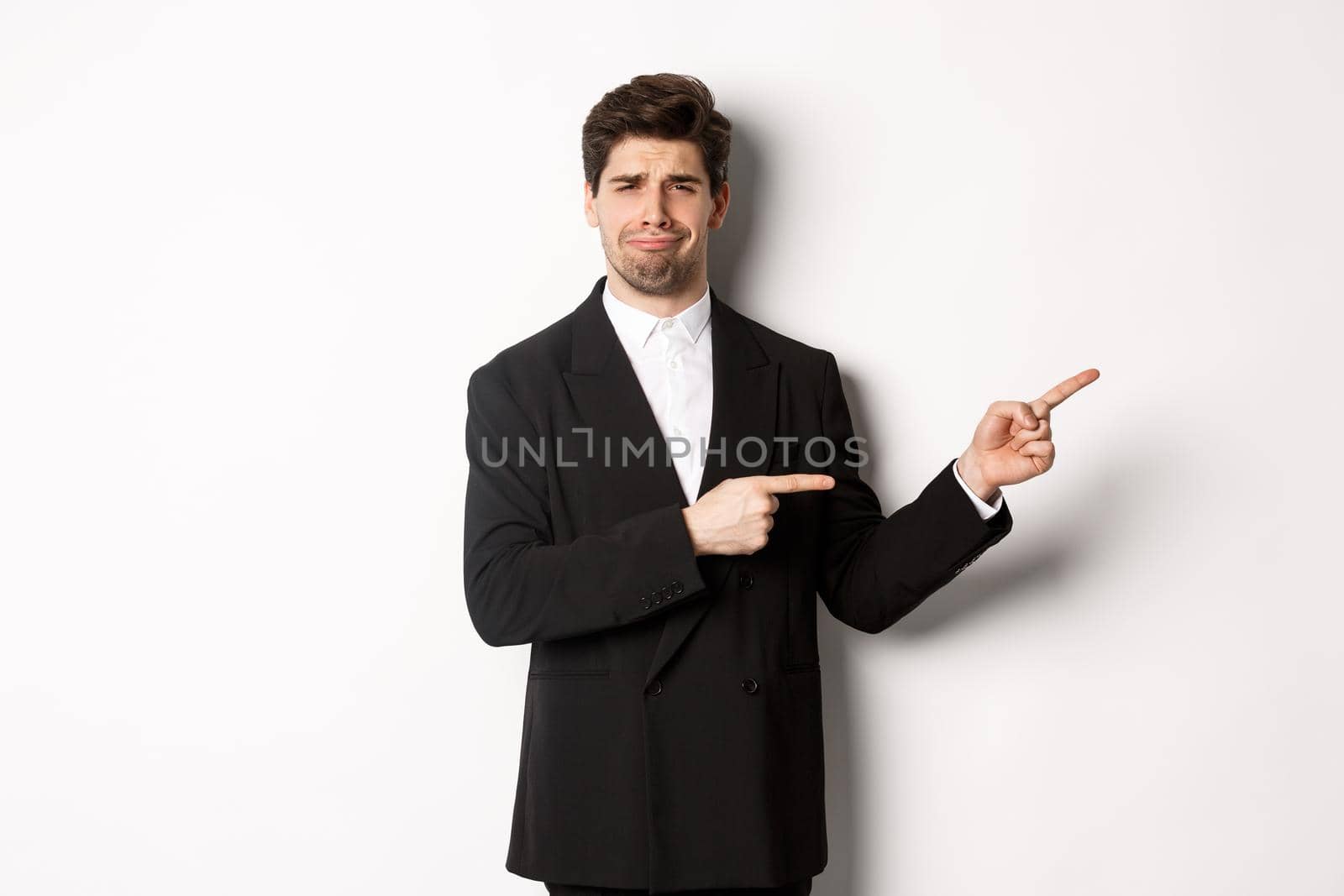 Image of devestated man in party suit, crying and complaining, pointing fingers right at something disappointing, standing over white background.