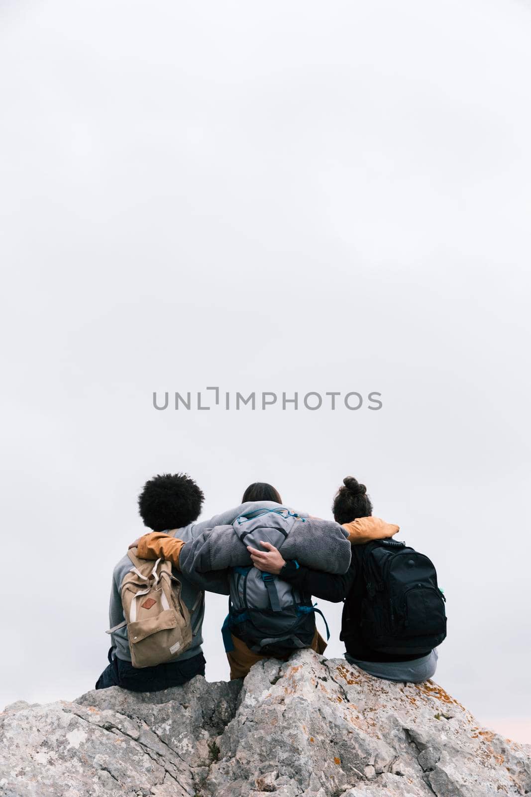 three friends with their arms around sitting top mountain. High quality photo by Zahard