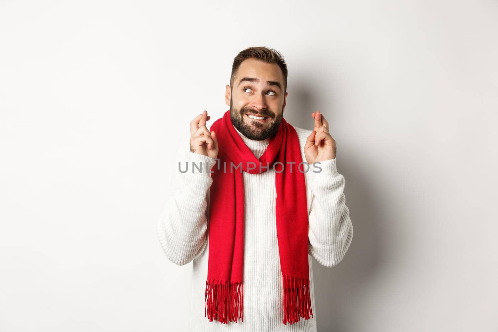 Christmas holidays and New Year concept. Hopeful man making wish with fingers crossed, waiting for gifts, standing over white background.