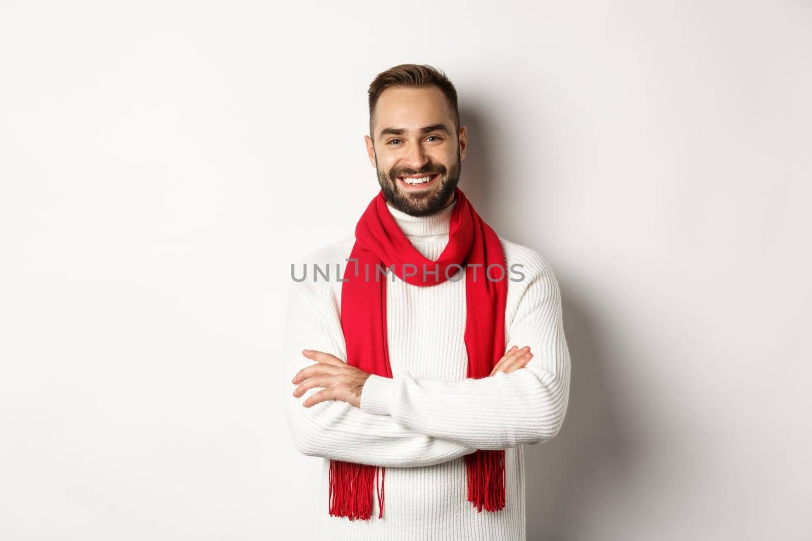 Christmas holidays and celebration concept. Handsome bearded man in sweater celebrating new year, wearing red scarf and smiling, standing over white background by Benzoix