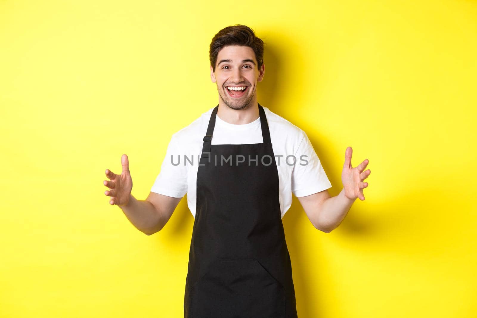 Happy barista holding something big, shaping large object, standing over yellow background.