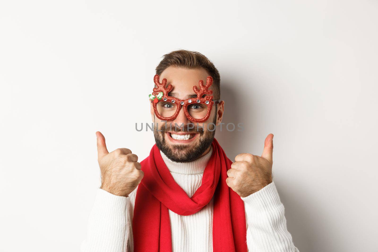 Christmas, New Year and celebration concept. Happy and satisfied man with beard, wearing party glasses, showing thumbs up in approval or like, standing over white background by Benzoix