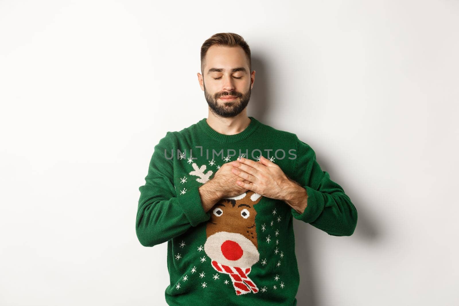 New year celebration and winter holidays concept. Young relaxed man feeling nostalgic, holding hands on heart and close eyes, dreaming about something on Christmas by Benzoix