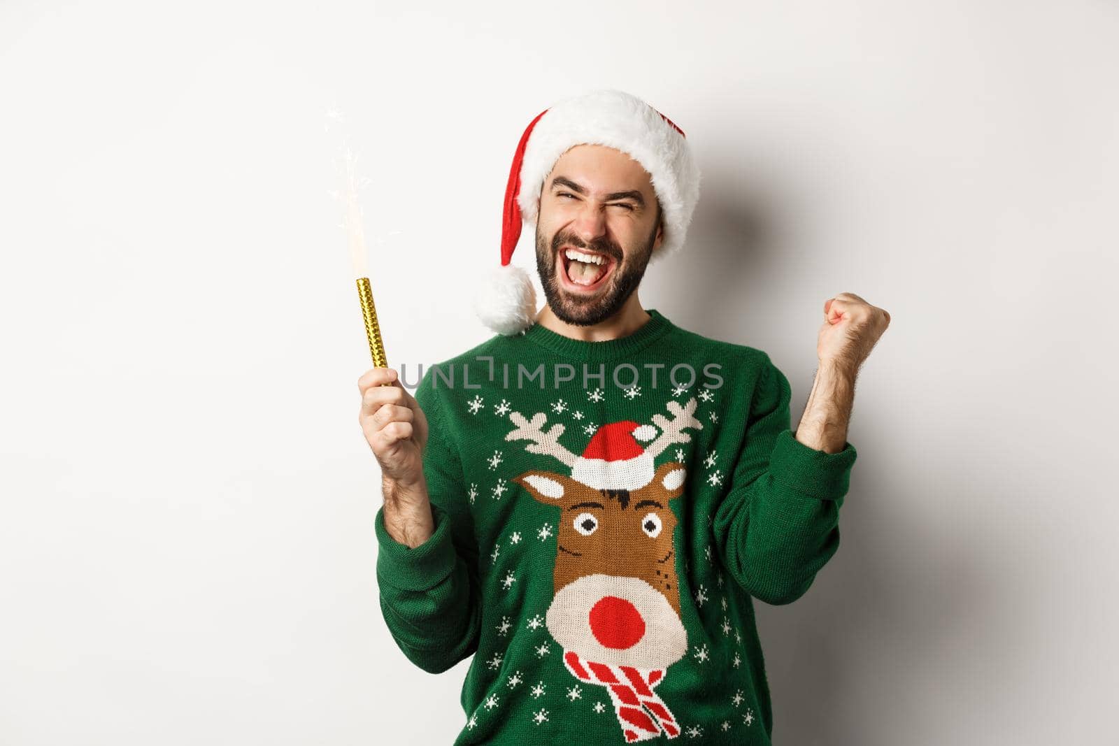 Christmas party and holidays concept. Happy young man celebrating New Year xmas, holding sparkler and looking excited, standing over white background.