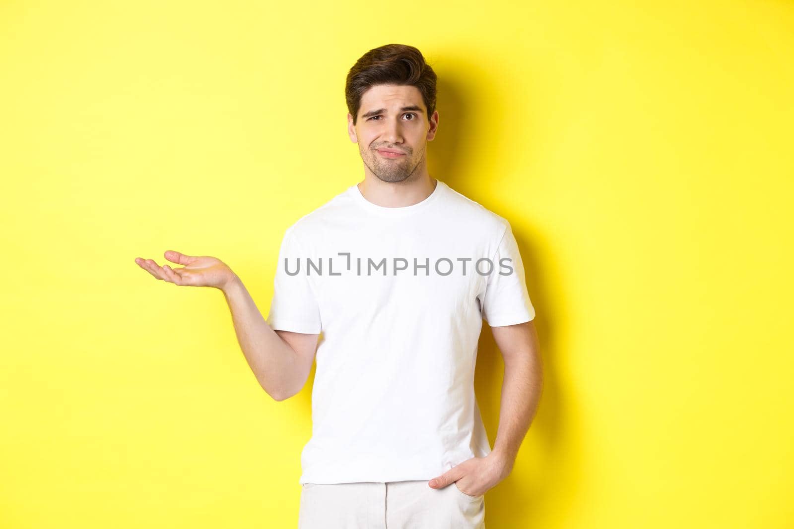 Confused and displeased guy raise hand, grimacing puzzled, standing against yellow background by Benzoix