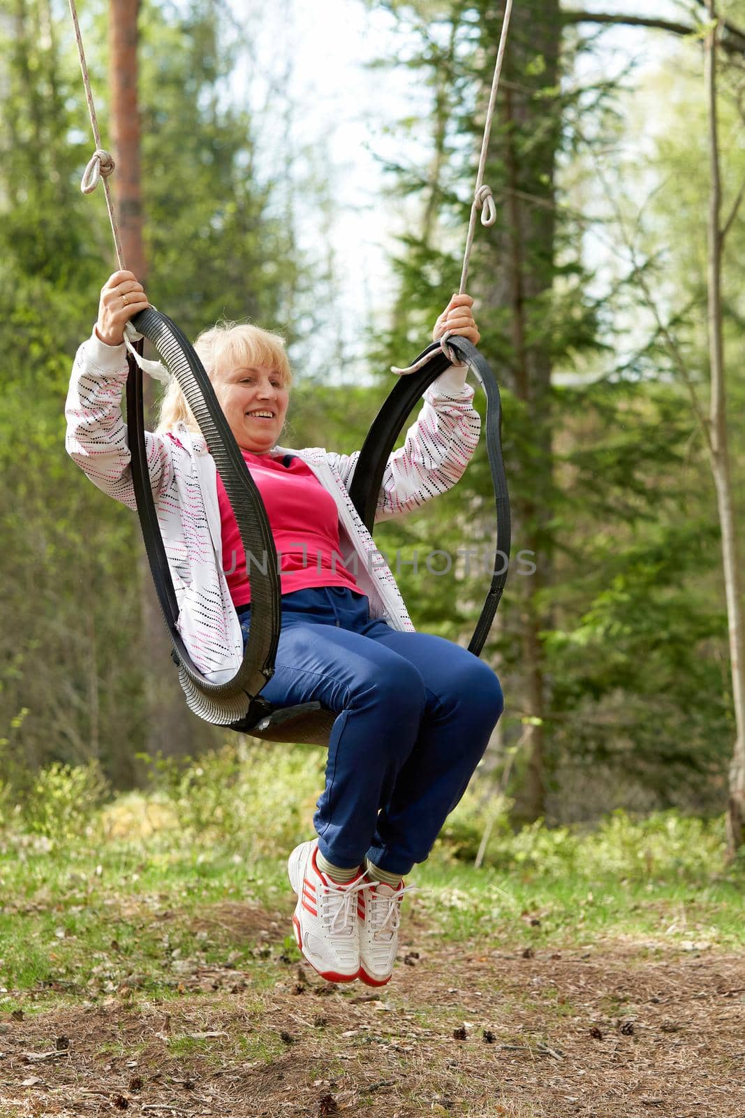 Middle aged woman in the woods swinging on a swing made from an old car tire by vizland