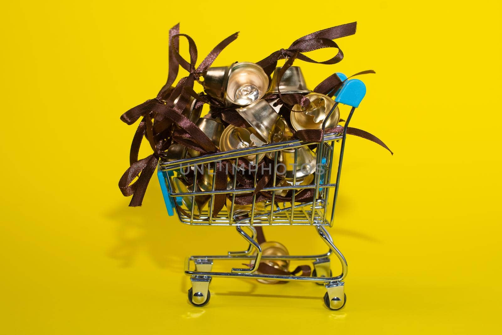 metal bells with ribbon bows in the shopping basket. on a yellow background. accessories for decoration.