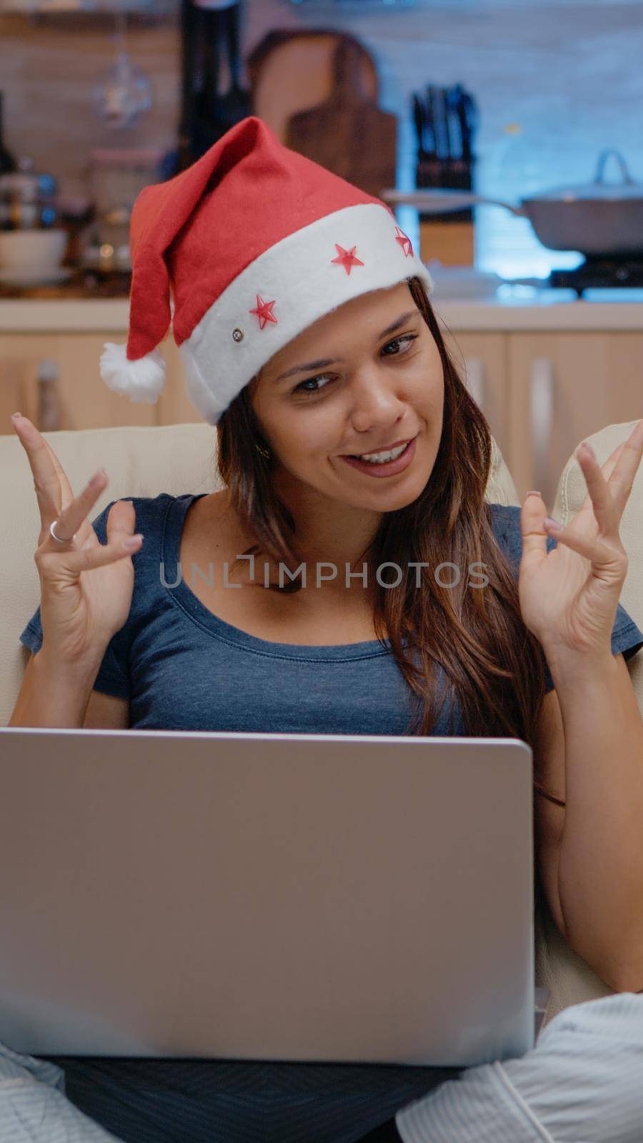 Person talking to family on video call conference to celebrate christmas eve. Woman wearing santa hat while using online conference for remote holiday festivity on laptop in festive room