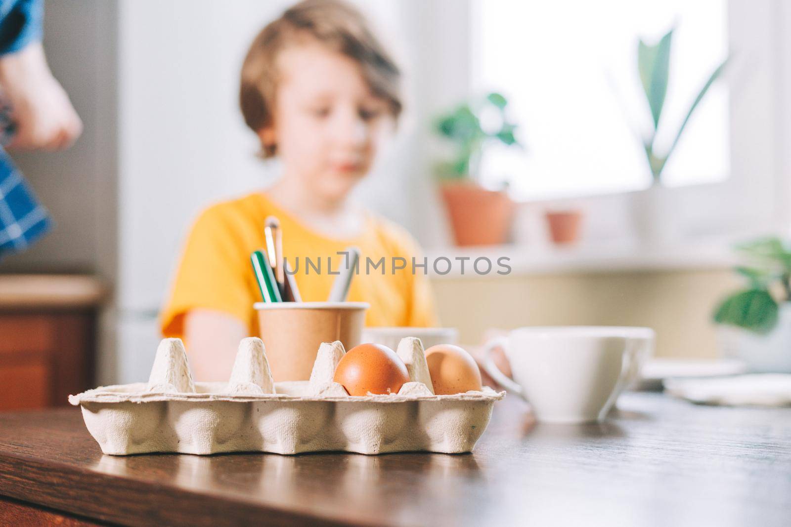 Easter day. Kid boy painting eggs on wooden background. Child sitting in a kitchen. Preparing for Easter, creative homemade decoration by Ostanina