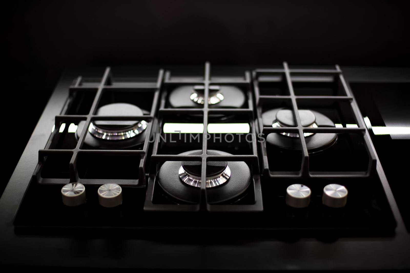 New modern black gas stove with four burners for the kitchen, stainless steel surface. Cast iron grates, top view, close up, black background.