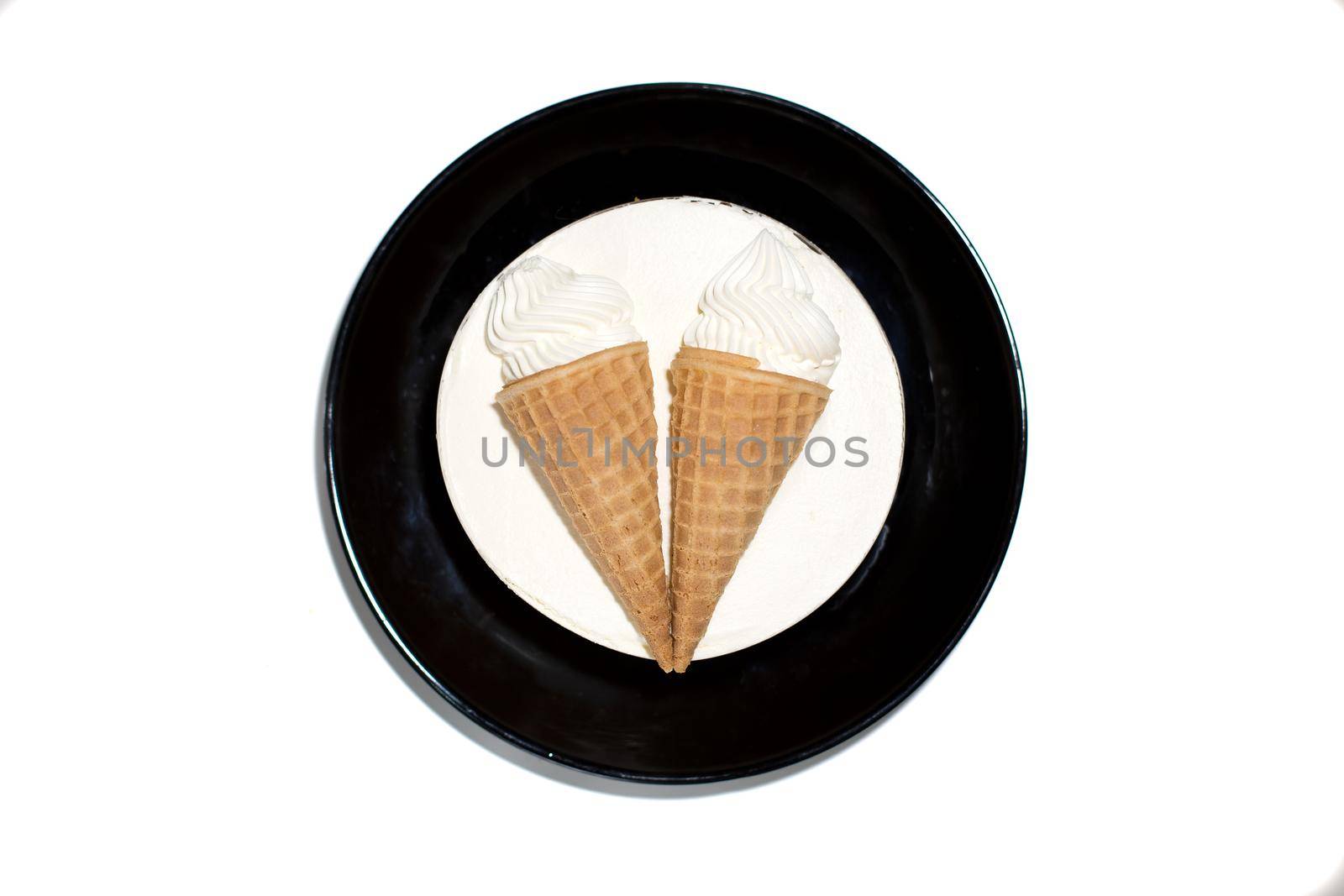 isolated round white dessert sweet delicious ice cream cake with decoration two ice cream cones in a waffle cup on a black plate. top view, close-up by Mariaprovector