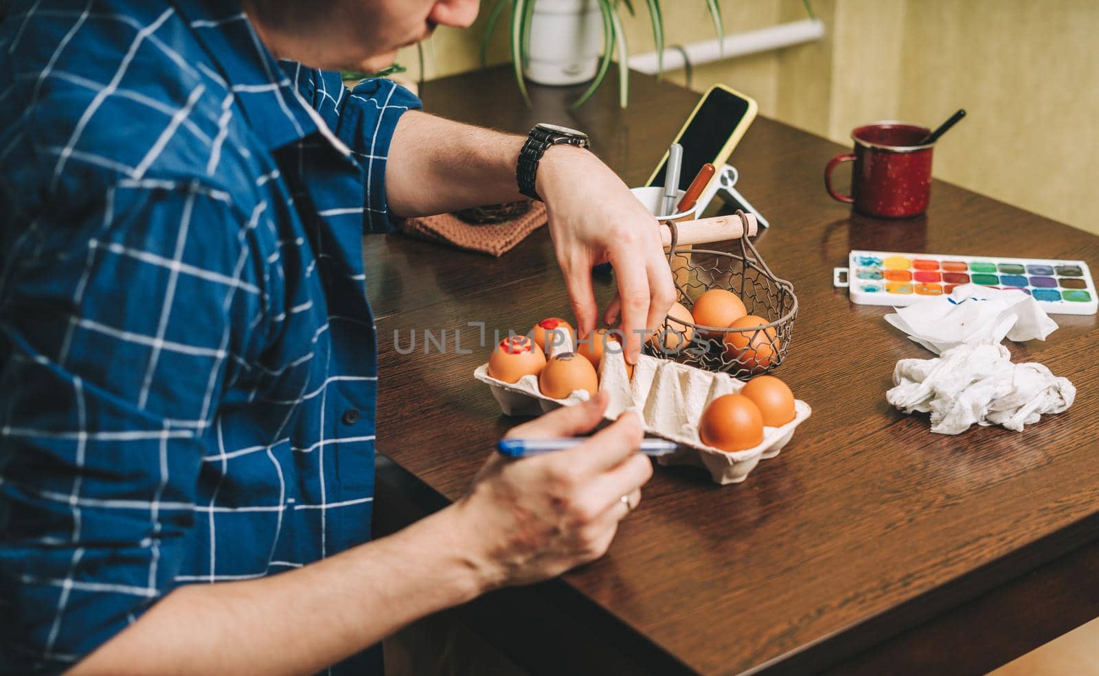 Easter day. Cropped Adult man painting eggs on wooden background. Sitting in a kitchen with paints. Preparing for Easter, creative homemade decoration for social media
