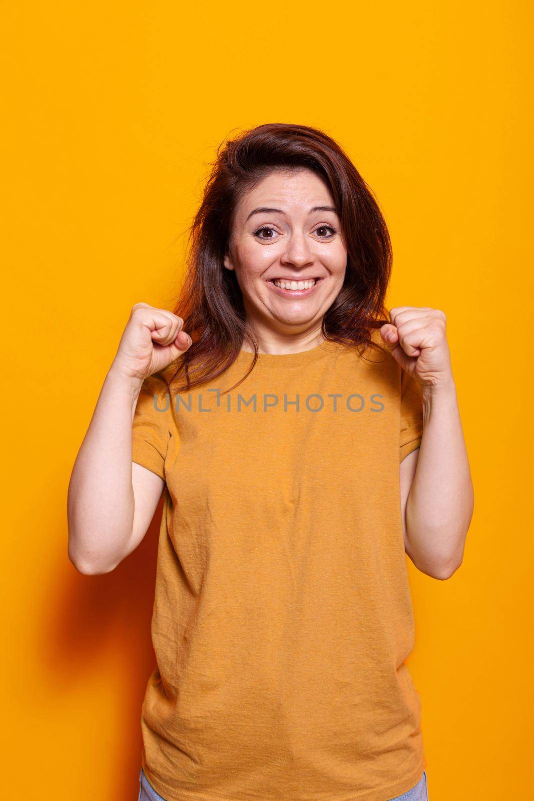 Joyful woman clenching fists and smiling in studio, hoping for good luck. Cheerful person doing hand gesture, having expectation about miracle in studio. Positive adult with desire