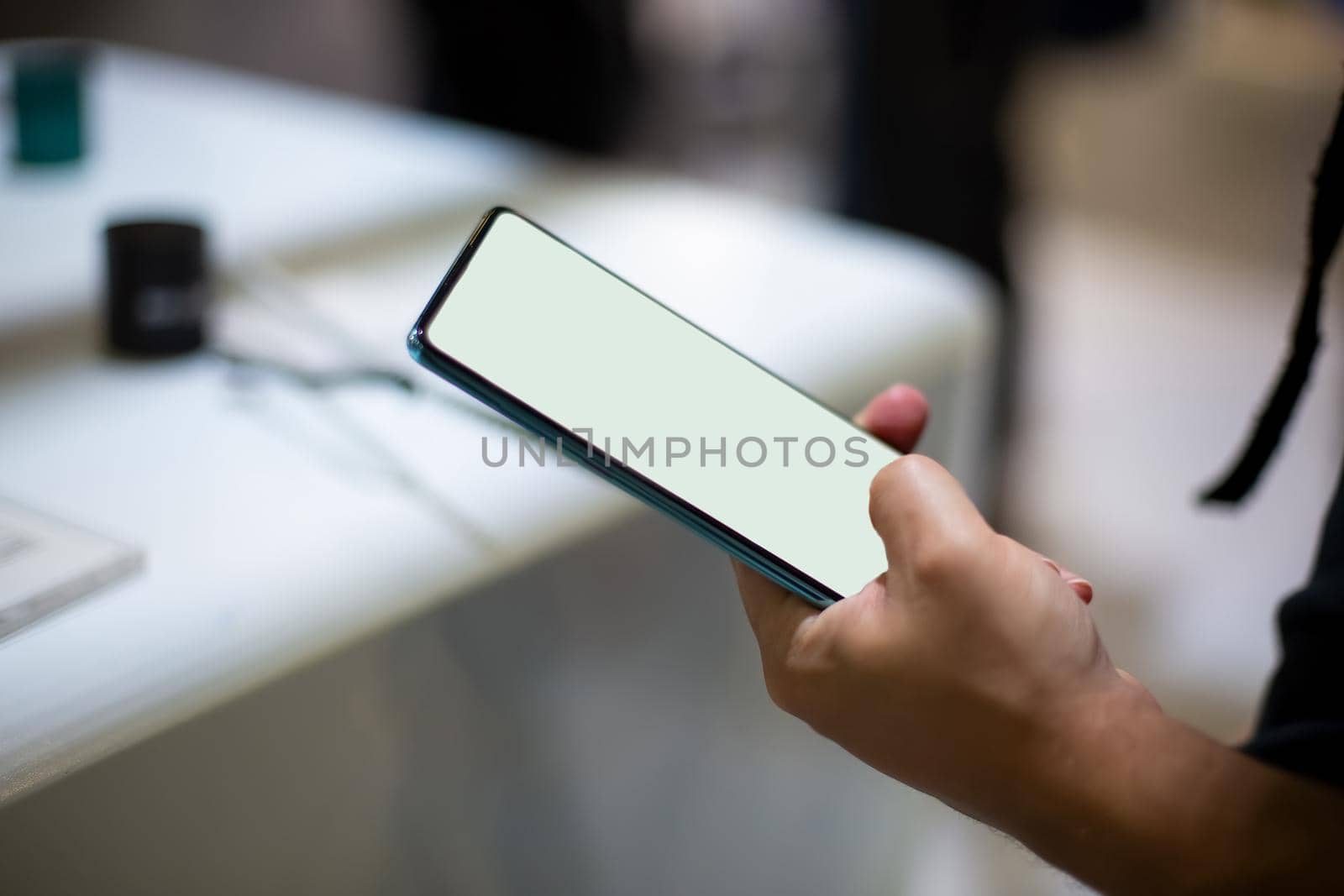 a caucasian man holds new smartphone with white screen copyspace. close up, soft focus. background in blur